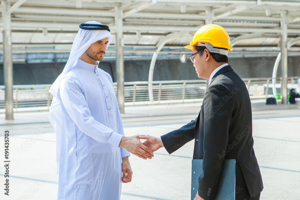 Arabic businessman shaking hands Asian Engineering over a deal negotiation to success with city background