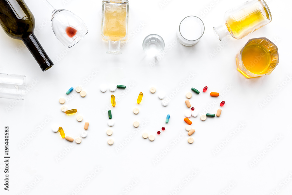 Alcoholism treatment. Glasses, bottles and pills. Word Stop on white background top view copy space Alcoholism treatment. Glasses, bottles and pills. Word Stop on white background top view copy space