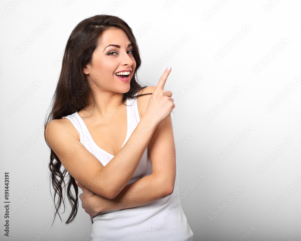 Beautiful excited casual woman pointing the finger up and smiling on white background Beautiful excited casual woman pointing the finger up and smiling on white background