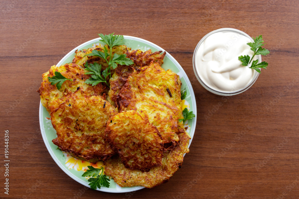 Homemade fried potato pancakes with sour cream on wooden table Homemade fried potato pancakes with sour cream on wooden table