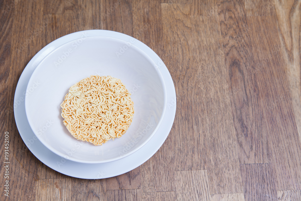 Uncooked Instant Noodles in white bowl and Plate on wooden table Uncooked Instant Noodles in white bowl and Plate on wooden table