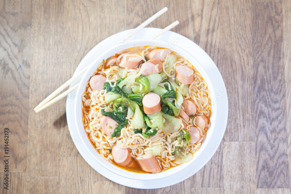 Instant Noodles with sausage with Pak Choy or Chinese Cabbage in white bowl and Plate on wooden table Instant Noodles with sausage with Pak Choy or Chinese Cabbage in white bowl and Plate on wooden table