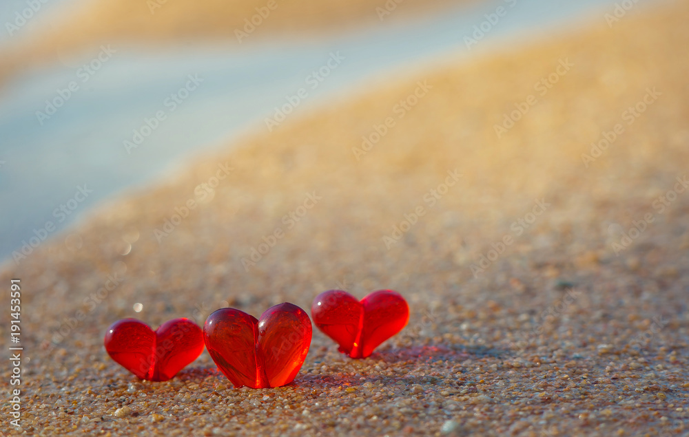 Fototapeta premium Three red glass heart lay on sand. Inner glow of light. Valentine day post card