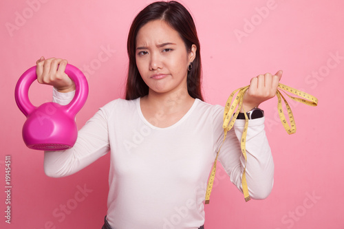 Exhausted Asian woman with dumbbells and measuring tape.