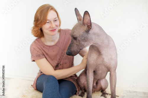 A woman stroking a Mexican Hairless Dog on a rug