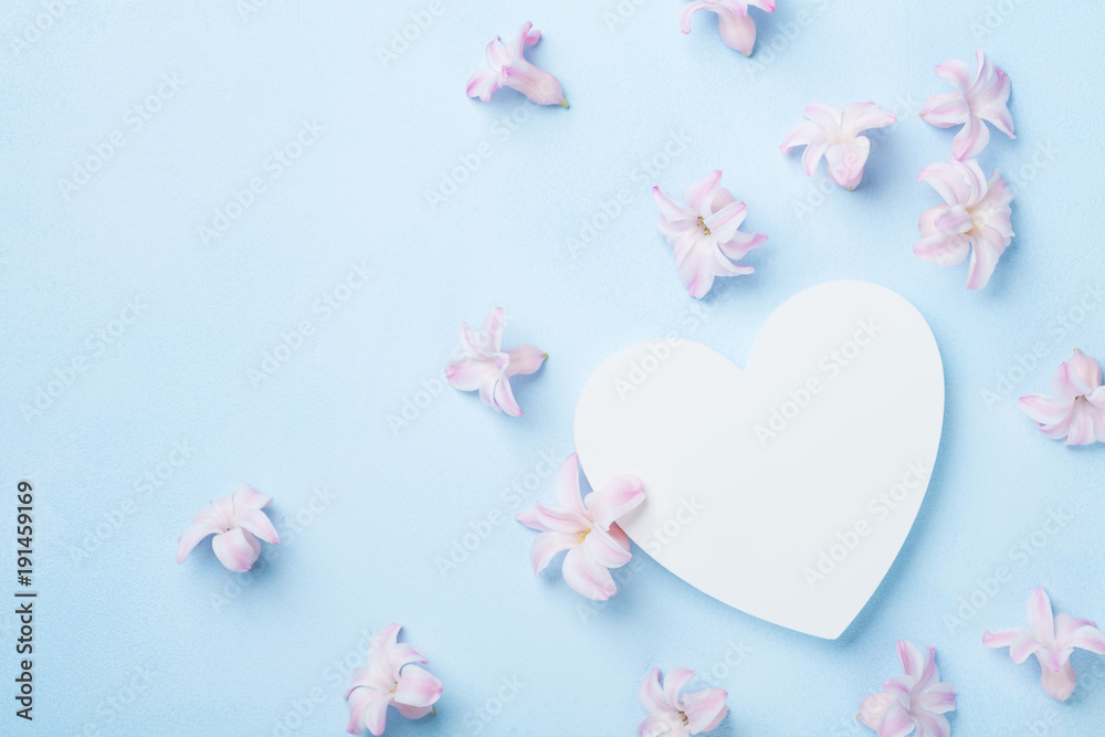 Wedding mockup with white heart and pink flowers on blue table from above. Beautiful floral pattern. Flat lay style.