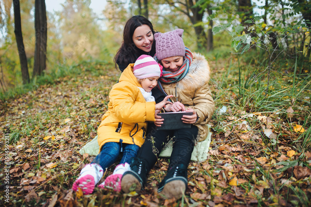 Friends are watching something interesting on the tablet. Autumn Park. Modern technology in nature. Fun and laughter. Friends are watching something interesting on the tablet. Autumn Park. Modern technology in nature. Fun and laughter.