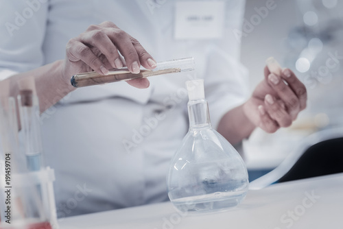 Proportions are important. Close up of female scientist holding a test tube and pouring a chemical liquid into a flask while working in a lab and conducting an experiment. © zinkevych