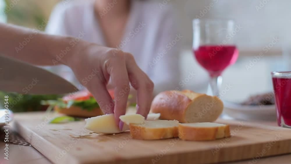 Woman putting sliced cucumber on sandwich on wooden board