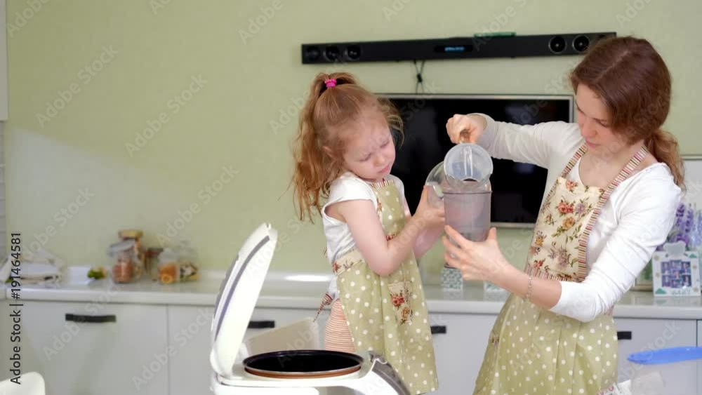 Young happy mother and her cute curly toddler daughterr in a kitchen to cook