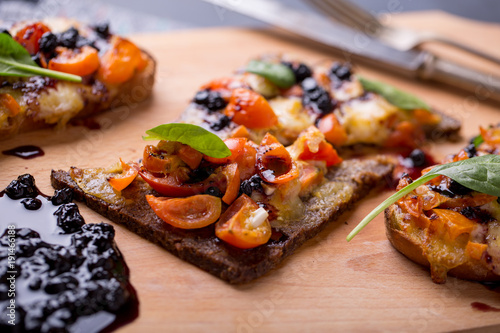 close up of delicious bruschetta with mozzarella, tomatoes and dark jam on a wooden plate
