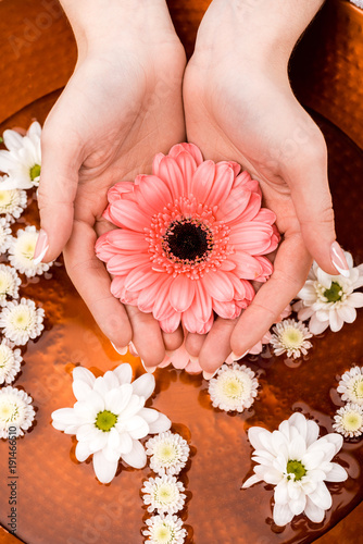 cropped view of woman making spa procedure with flowers in beauty salon, nail care concept