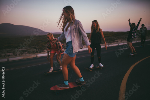 Group of young adult friends cheering and riding longboards photo