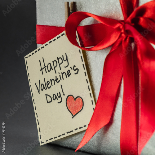 Gift in silver packaging with red ribbon and greetings with Valentine's day.