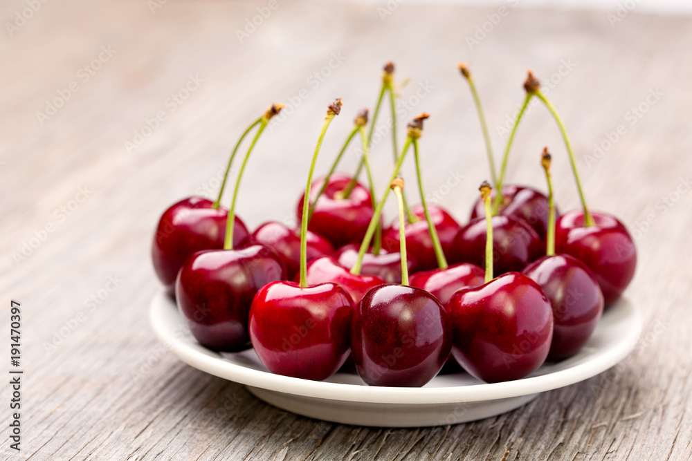 Ripe cherries on a white plate on a wooden table Ripe cherries on a white plate on a wooden table