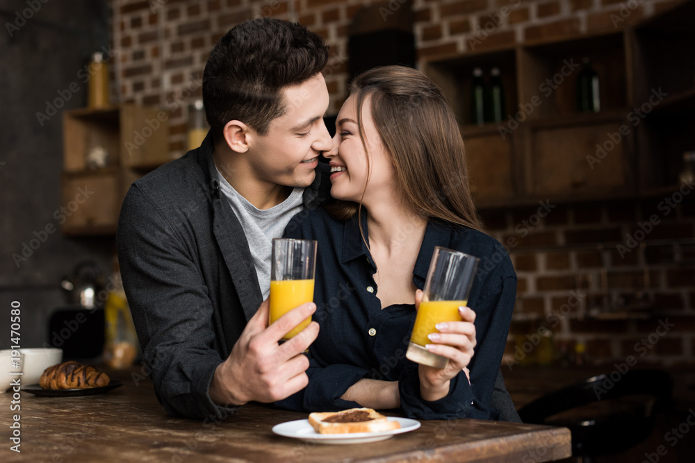 smiling couple with orange juice going to kiss at kitchen