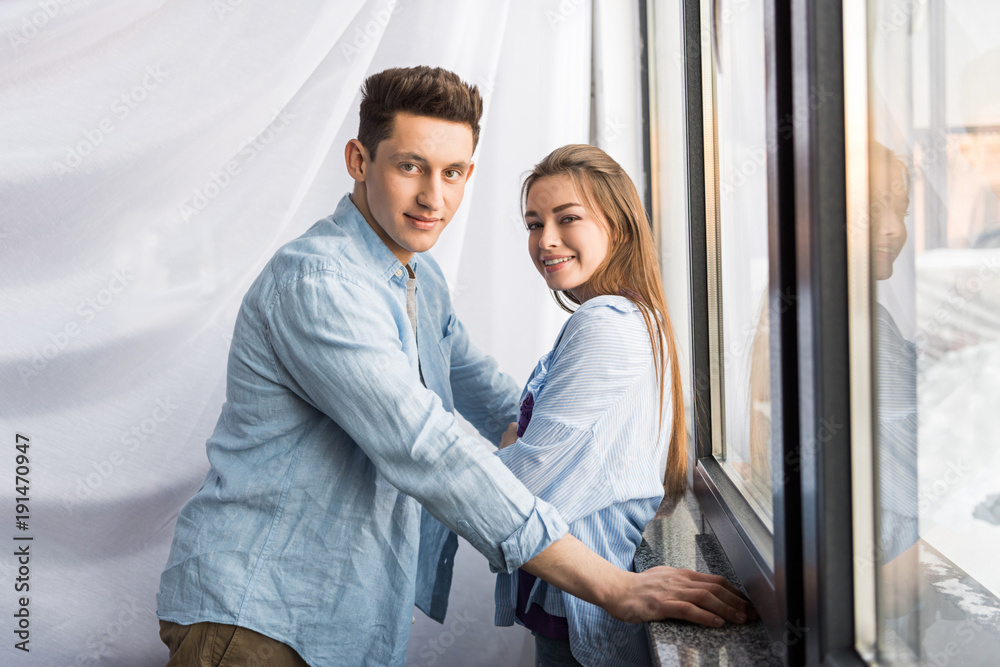 happy couple near window looking at camera happy couple near window looking at camera