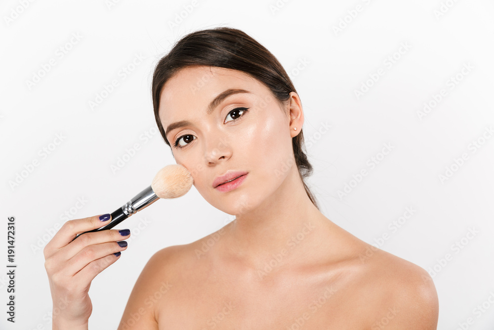 Close up studio portrait of beautiful asian woman with soft skin applying makeup with brush isolated over white background Close up studio portrait of beautiful asian woman with soft skin applying makeup with brush isolated over white background