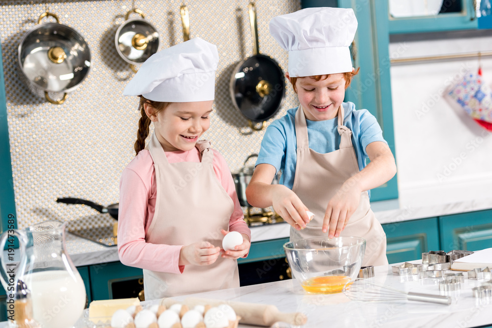 cute smiling kids in chef hats and aprons preparing dough together in kitchen cute smiling kids in chef hats and aprons preparing dough together in kitchen
