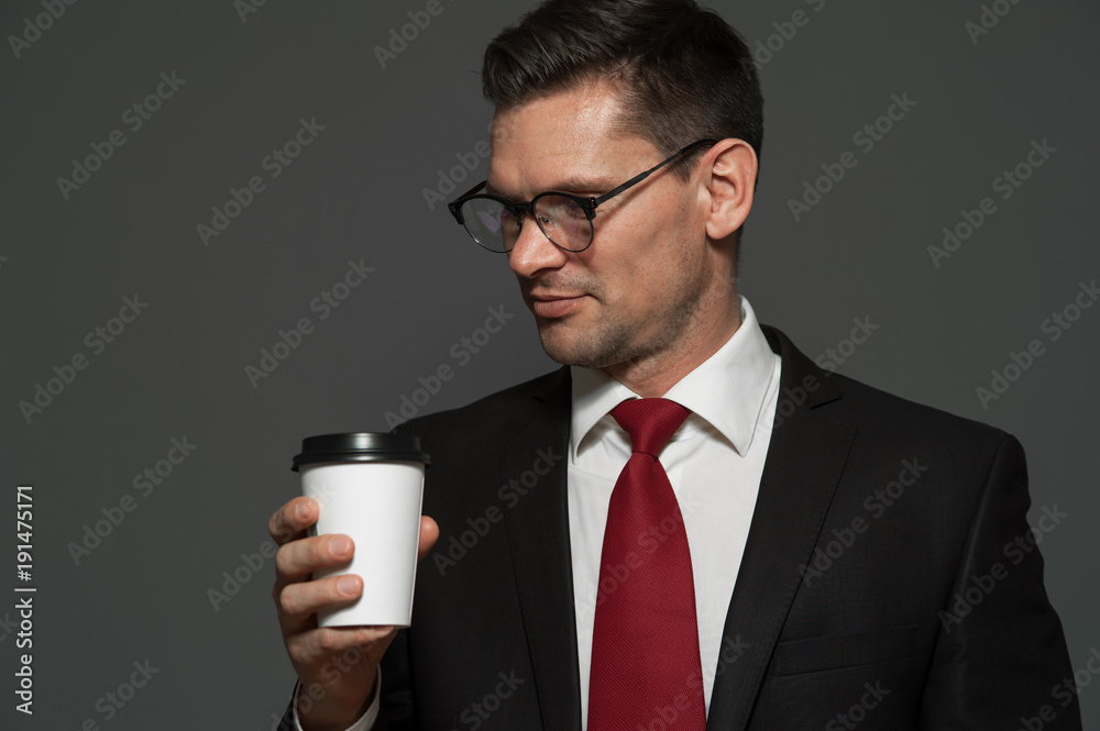 Close-up - young male manager in formal attire and glasses is drinking coffee on gray background Close-up - young male manager in formal attire and glasses is drinking coffee on gray background