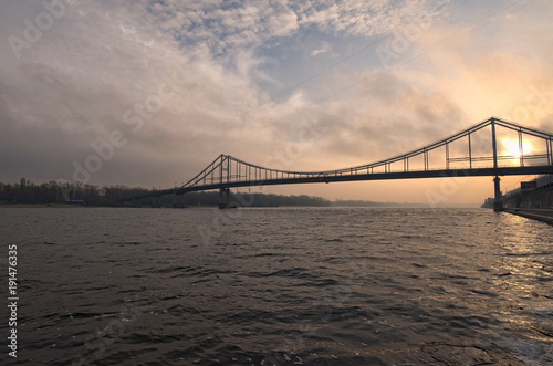Pedestrian bridge to the Trukhanov island in Kyiv through the Dnipro River in the sunrise. Winter morning. Ukraine. Selective focus with wide angle lens