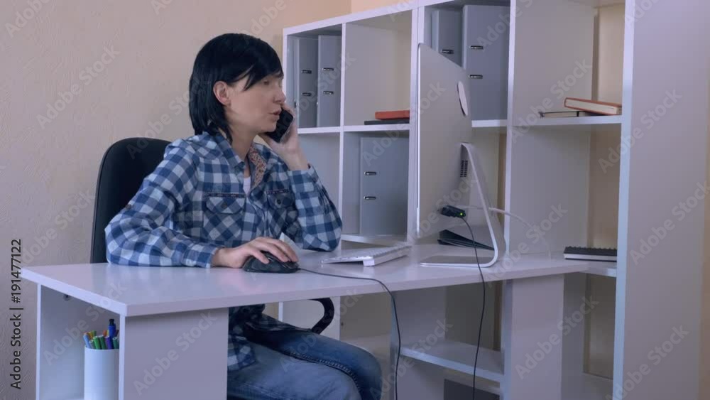 worker use mobile at work cheerful businesswoman has phone conversation brunette wearing casual shirt looking on display. using computer and smartphone