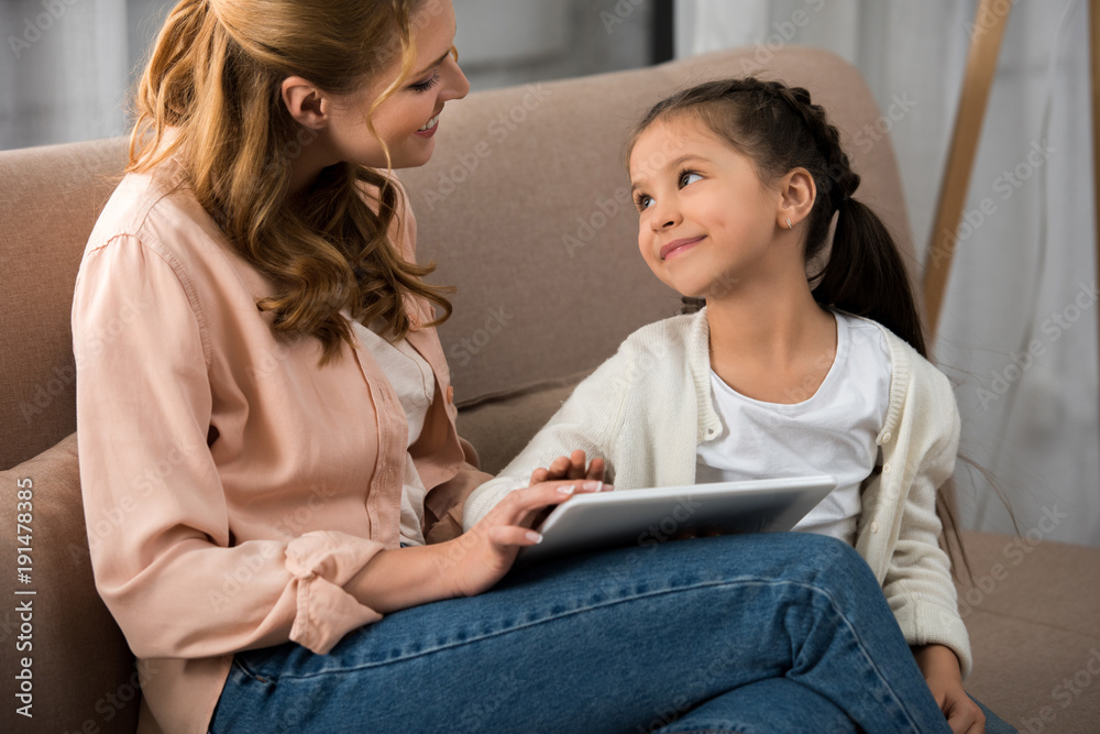 happy mother and daughter smiling each other while using digital tablet at home happy mother and daughter smiling each other while using digital tablet at home