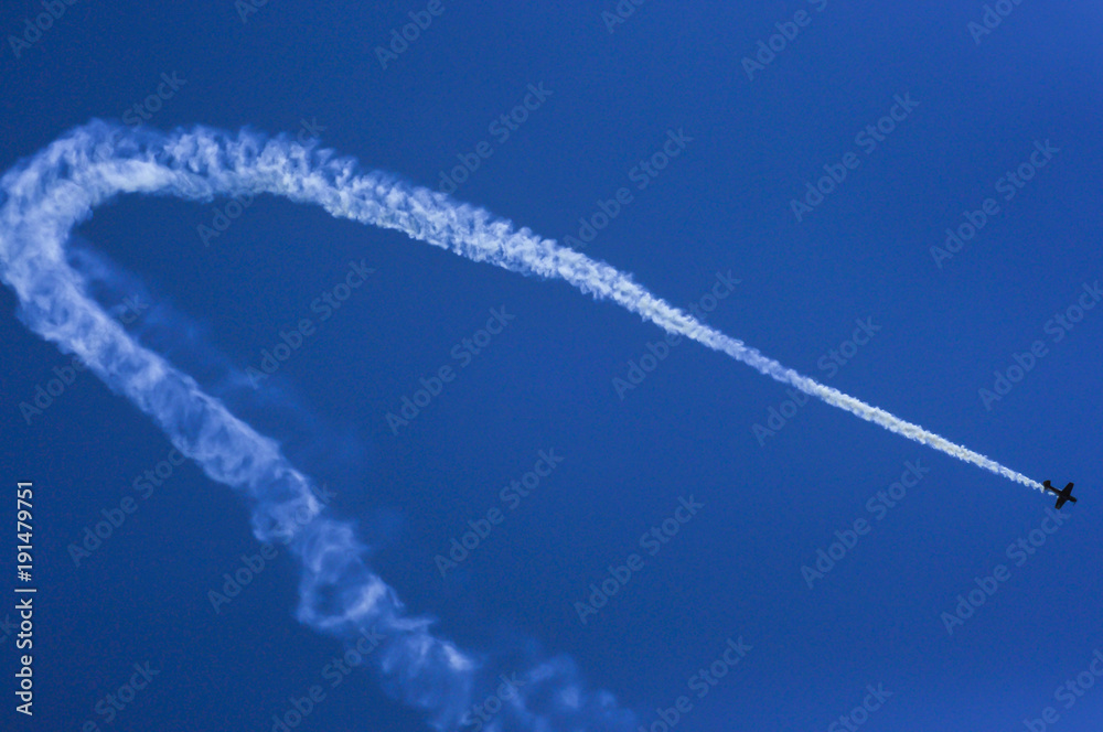 Small airplane leaving a trail of smoke with the blue sky in the background Small airplane leaving a trail of smoke with the blue sky in the background
