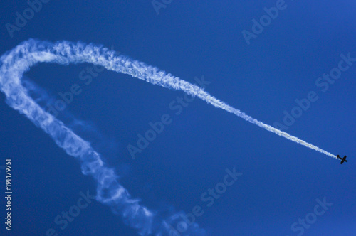 Small airplane leaving a trail of smoke with the blue sky in the background © Marian