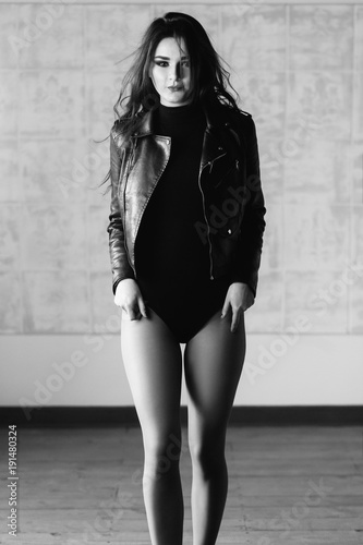 Sexy woman in leather jacket with naked legs poses on the chair in a studio