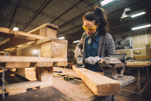 Fotografi Portrait view of hardworking middle aged professional female carpenter worker working with sandpaper and choosing wood in the workshop