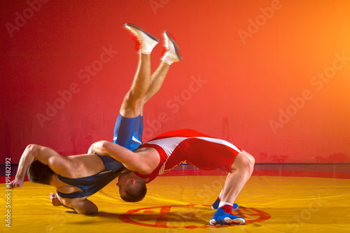 Canvas Print Two  strong men in blue and red wrestling tights are wrestlng and making a suplex wrestling on a yellow wrestling carpet in the gym