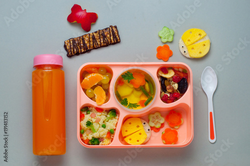 Lunch box with fruits, soup, couscous salad and funny sandwiches on grey background