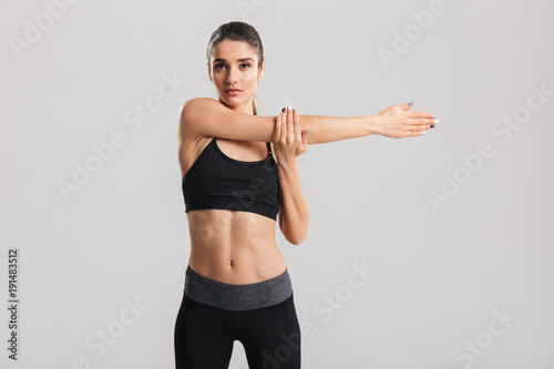 Picture of slim beatiful woman doing aerobic exercise and stretching her body, isolated over gray background © Drobot Dean