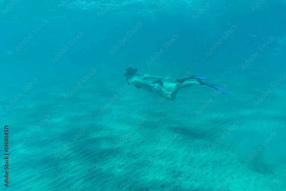 Beautiful woman underwater in Bikini snorkels over coral reef in the Sea