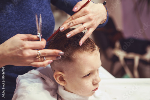 Little boy at the hairdresser. Child is scared of haircuts. Hairdresser's hands making hairstyle to little boy, close up
