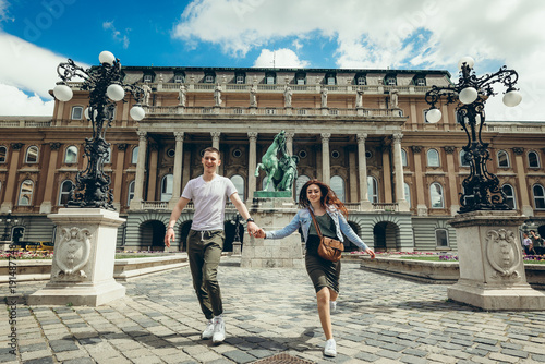 Full-length view of the pretty young couple in love holding hands while walking along the countryard at the Buda Castle Royal Palace in Budapest, Hungary. photo
