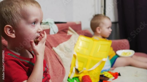 The brothers sit on the sofa at home and watch TV. Eat corn sticks and smile
