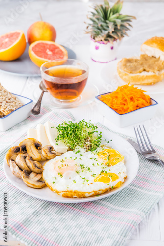 Healthy breakfast plate with scrambled eggs, cheese, grilled mushrooms and sprout micro greens and other snacks and drinks on the served white wooden table. Selective focus.