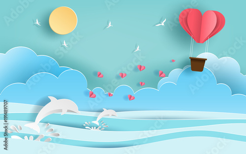 Paper art style of origami heart shaped hot air balloon flying in the air over beautiful beach with many hearts floating, flat-style vector illustration.