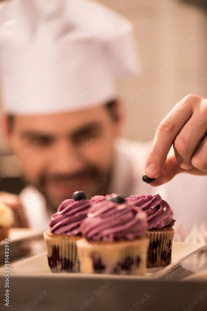 selective focus of confectioner decorating cupcakes with berries in restaurant kitchen