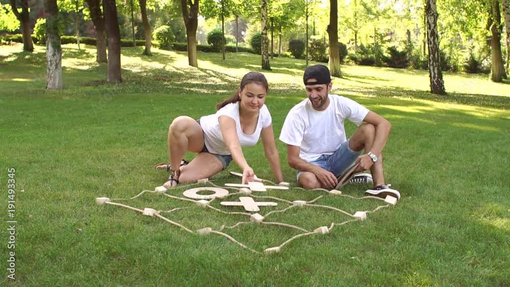 Two young people play the game tic tac toe big pieces in the Park in the summer. Large outdoor games.