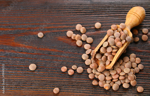 Red lentils in a wooden scoop on a wooden table.