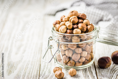 Peeled hazelnuts in a glass jar on white wooden background. Selective focus, space for text.