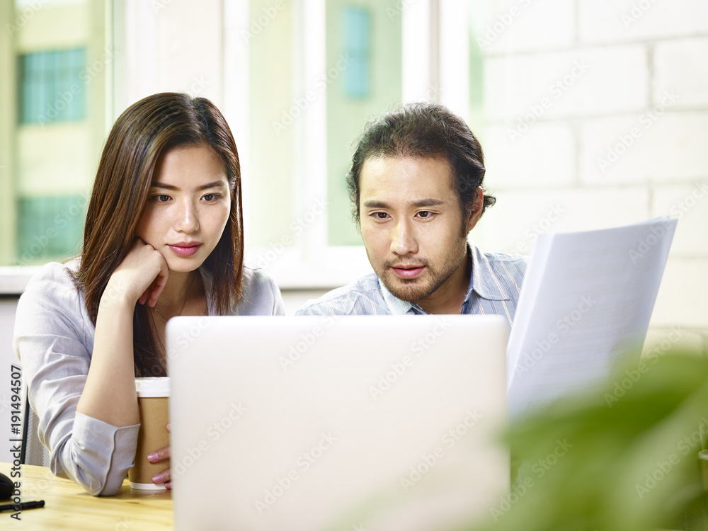 asian businessman and businesswoman working together in office using laptop computer