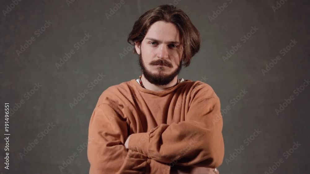 Portrait of serious, handsome man with a dark beard, wearing casual orange shirt, indoor shot in the gray background Portrait of serious, handsome man with a dark beard, wearing casual orange shirt, indoor shot in the gray background