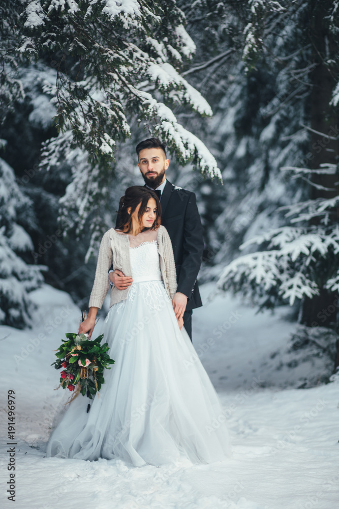 Bearded man and his lovely bride pose on the snow in a magic winter forest Bearded man and his lovely bride pose on the snow in a magic winter forest