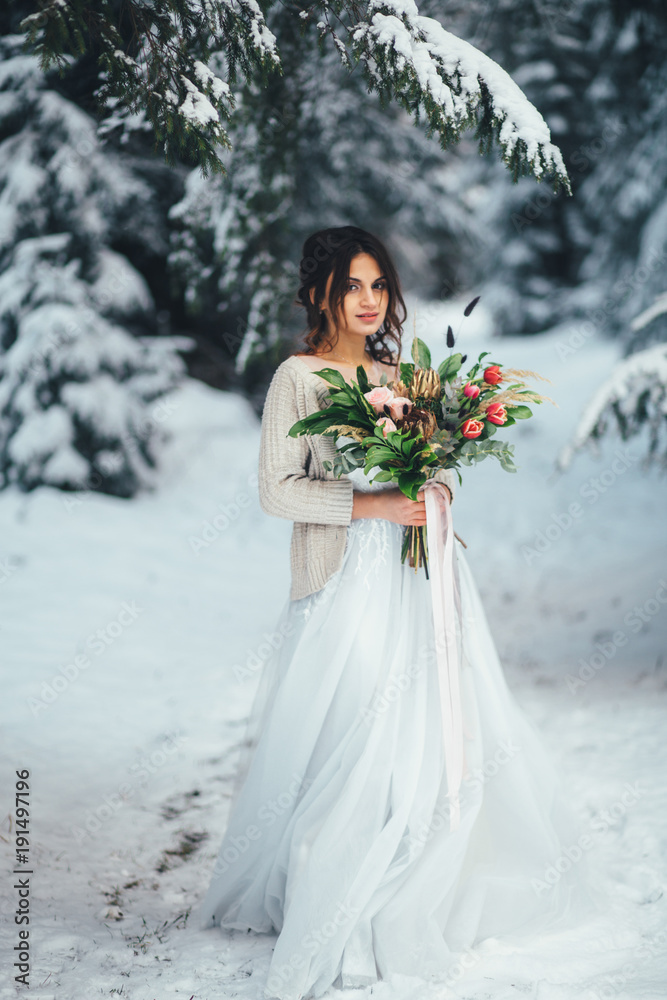 Lovely bride poses with rich wedding bouquet in a winter forest Lovely bride poses with rich wedding bouquet in a winter forest