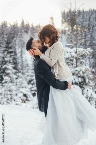 Bearded man and his lovely bride pose on the snow in a magic winter forest