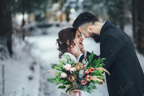 Bearded man and his lovely bride pose on the snow in a magic winter forest